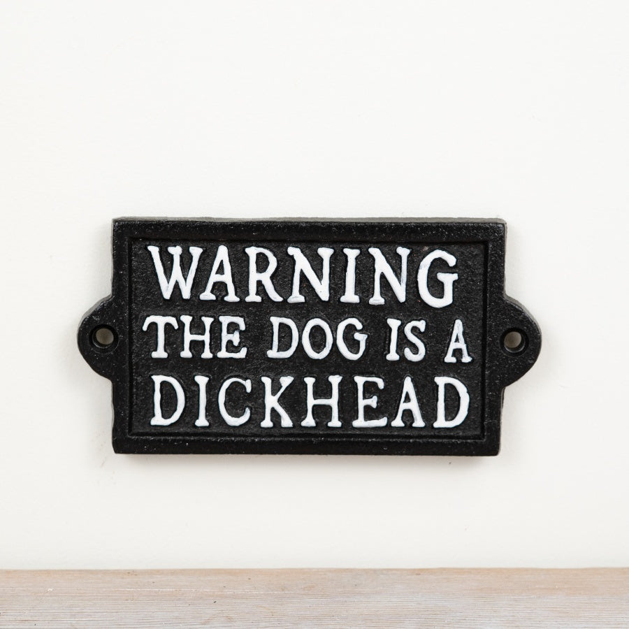 Cast iron sign reading “Warning The Dog Is A Dickhead” with rustic vintage-style humorous design.