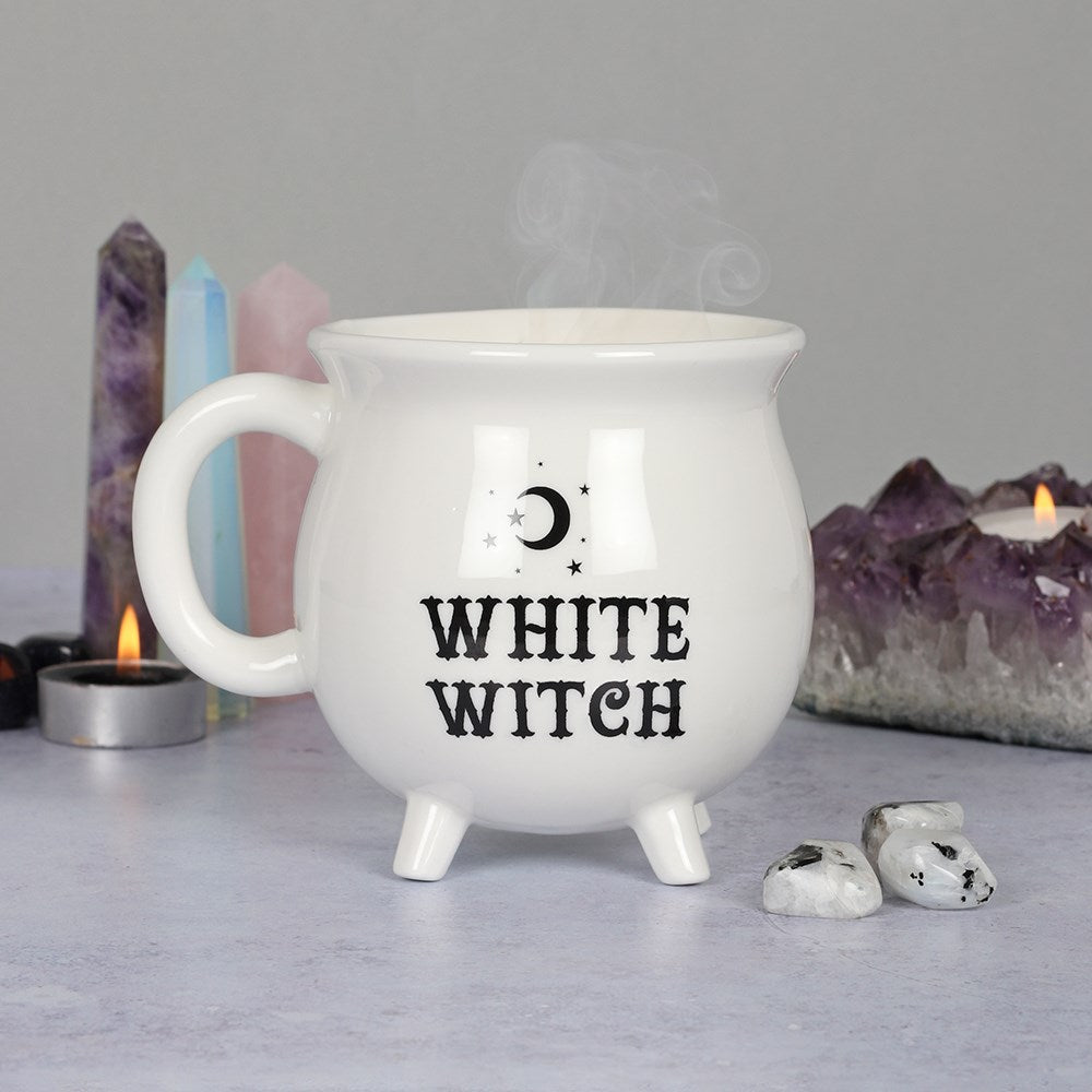 White ceramic cauldron-shaped mug with White Witch text and crescent moon detail, styled with amethyst crystals, crystal towers and tealight candles