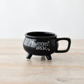 Black ceramic Witch's Brew cauldron mug with three legs, square handle and white star detailing, on a wooden surface